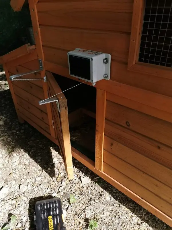 Montage d'un module de fermeture automatique et solaire sur une porte de poulailler en bois.